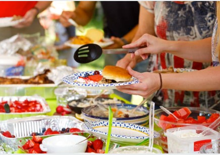 Hands serving food at a buffet with various dishes.