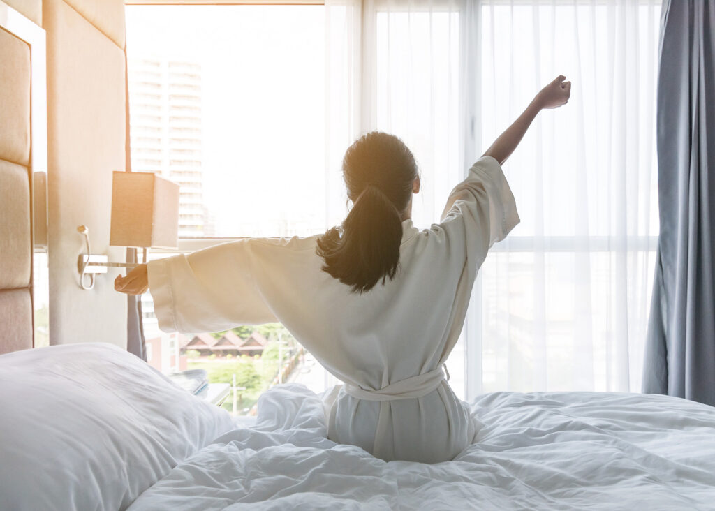 Woman in a white bathrobe stretching on a bed 